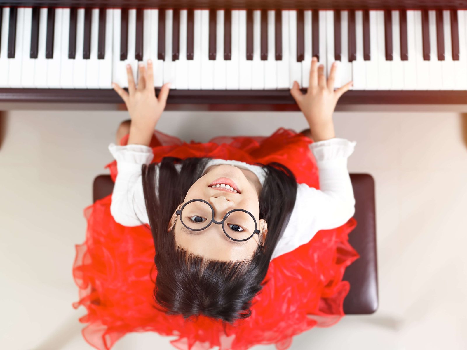 A young girl at an upright piano, looking up from the keys.