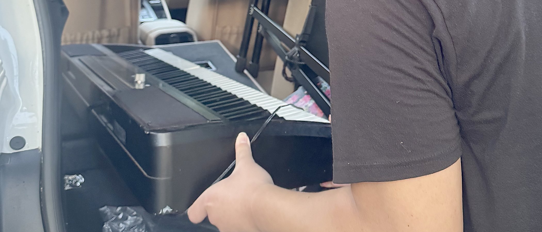 A student steadying a donated digital piano in the back of a car.