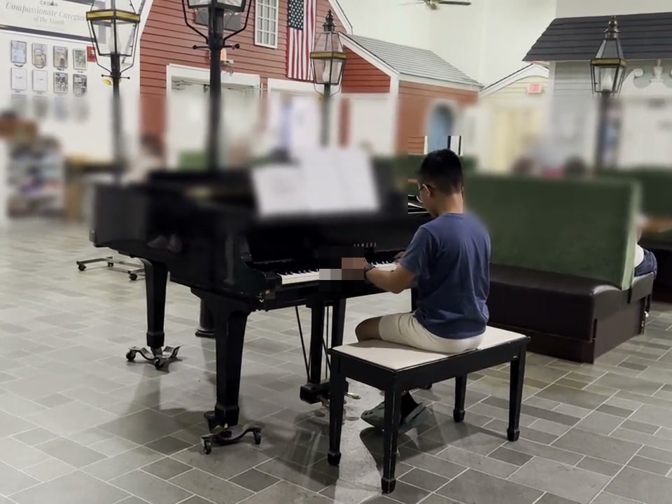 A student playing a grand piano in a senior community common room.