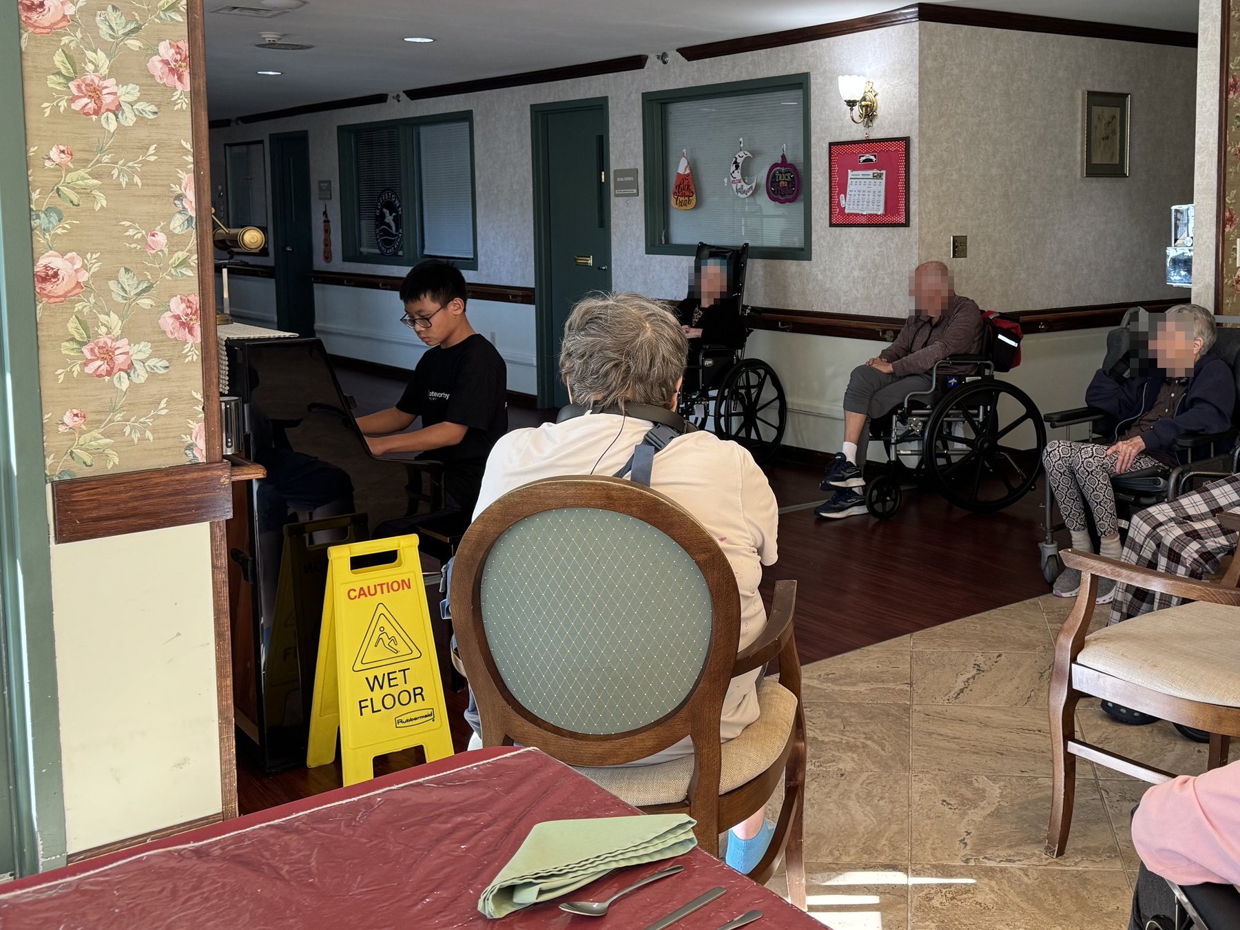 A student playing the piano for residents seated along a hallway.