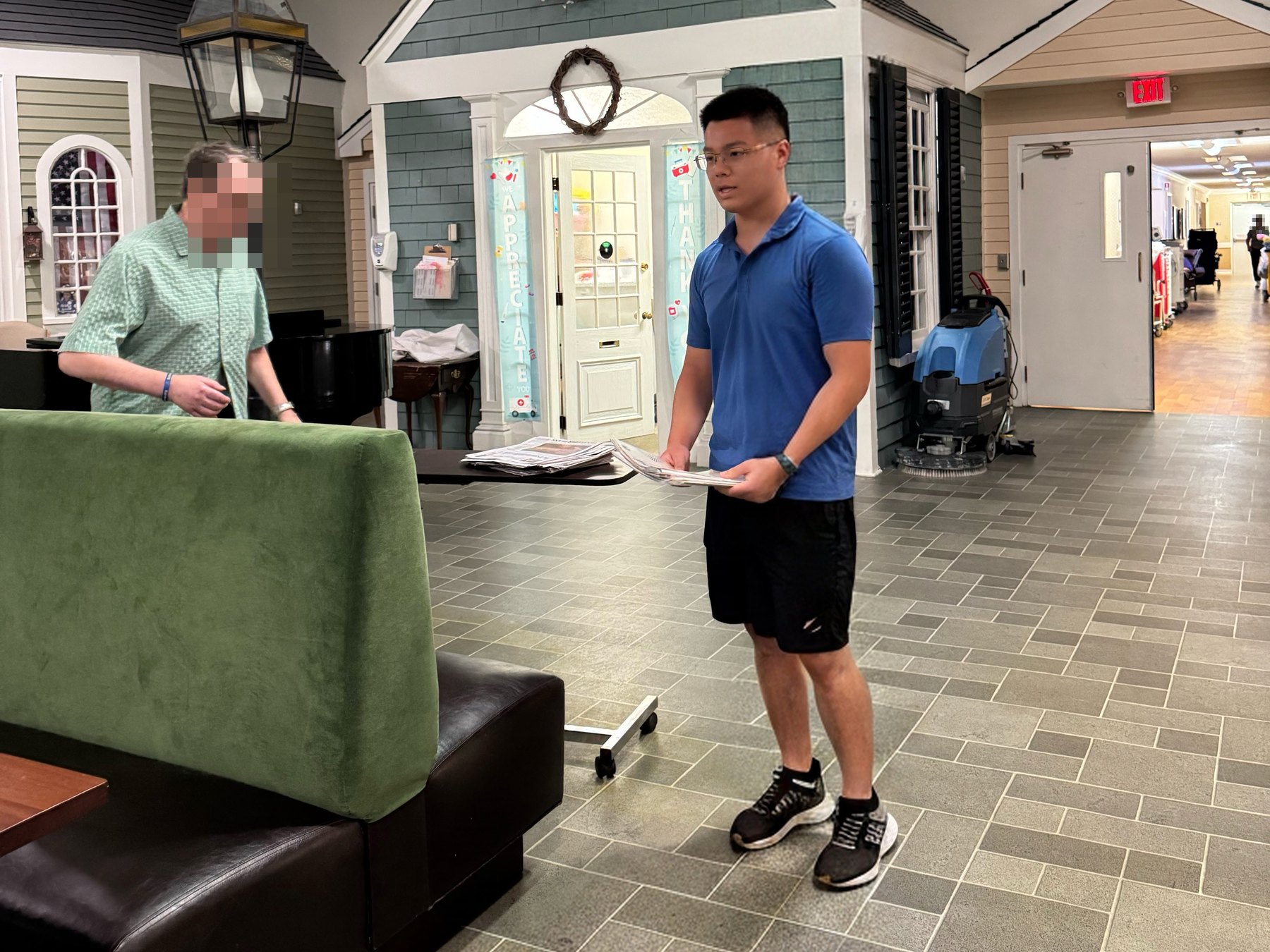 Ethan talking with someone in a residence common room after playing, sheet music still in his hand.